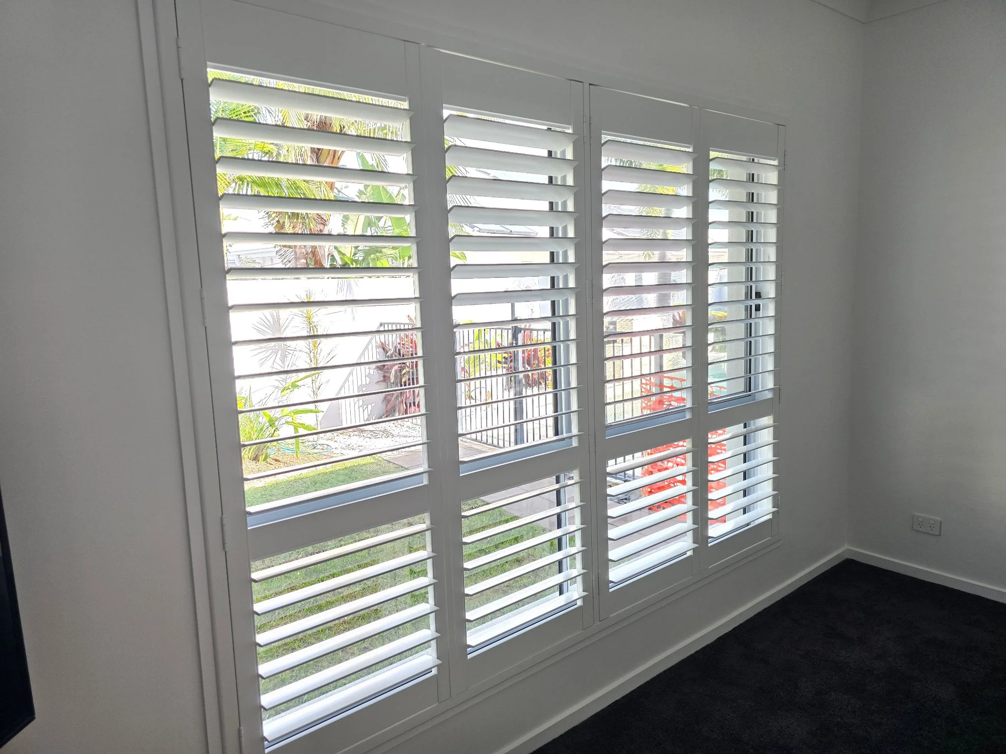 Plantation shutters on bedroom window with a view of the back yard and pool